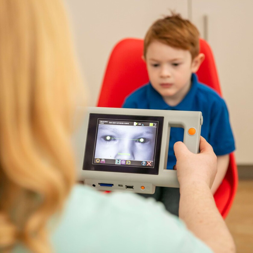 Augenarzt f&uuml;hrt mit einem Hand-Autorefraktometer einen Sehtest bei einem kleinen Jungen durch.