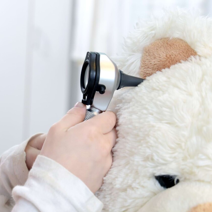 Kinderh&auml;nde untersuchen das Ohr eines wei&szlig;en Teddyb&auml;ren mit einem Otoskop.
