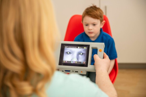 Augenarzt f&uuml;hrt mit einem Hand-Autorefraktometer einen Sehtest bei einem kleinen Jungen durch.