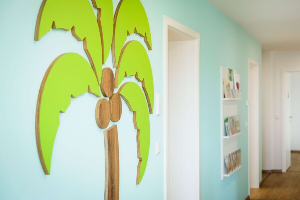 Gro&szlig;e Wanddekoration als Palme mit gr&uuml;nen Bl&auml;ttern und h&ouml;lzernem Stamm an einer hellblauen Flurwand.