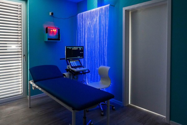 Blau beleuchtetes Untersuchungszimmer mit Liege, Ultraschallger&auml;t und beruhigendem Lichtvorhang.