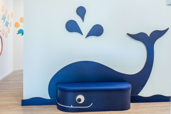 Blaue Kindersitzbank in Form eines Wals vor hellblauer Wand mit Wassertropfen-Deko.