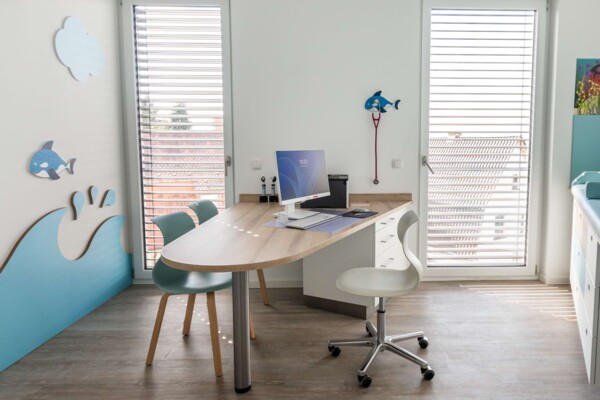 Helles Sprechzimmer mit Holzschreibtisch, blauen St&uuml;hlen und maritimer Wanddeko mit Wellen und Walen.