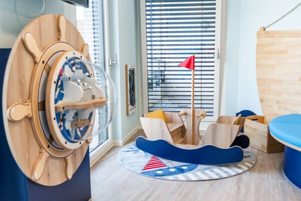 Helles Spielzimmer im maritimen Stil mit gro&szlig;em Holz-Steuerrad, Schaukelboot und rundem Teppich.